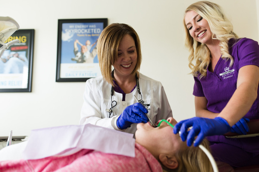 Two women in a dental office, one holding a mouth open for an examination while the other appears to be conducting the procedure.